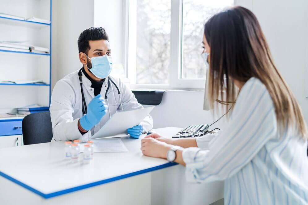 A doctor wearing a face mask consults with a patient in a modern clinic, discussing allergy symptoms and treatment options. The image reflects professional, personalized healthcare and allergy specialist consultation.