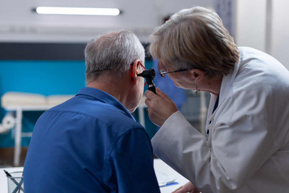 An ENT specialist examines an older patient’s ear using an otoscope during a clinical consultation.