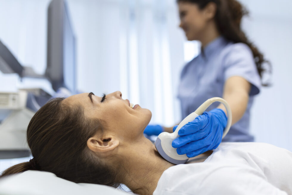 A patient undergoes a thyroid ultrasound examination while a healthcare professional uses an ultrasound probe on the neck.