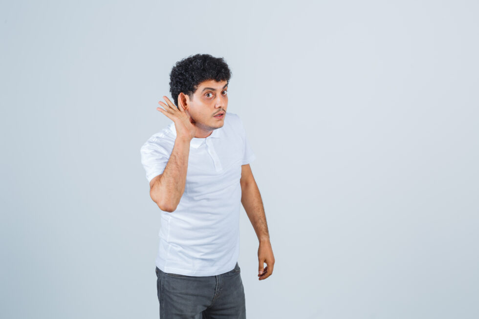 A man cups his hand around his ear, showing difficulty hearing and highlighting a possible early sign of hearing loss in adults.