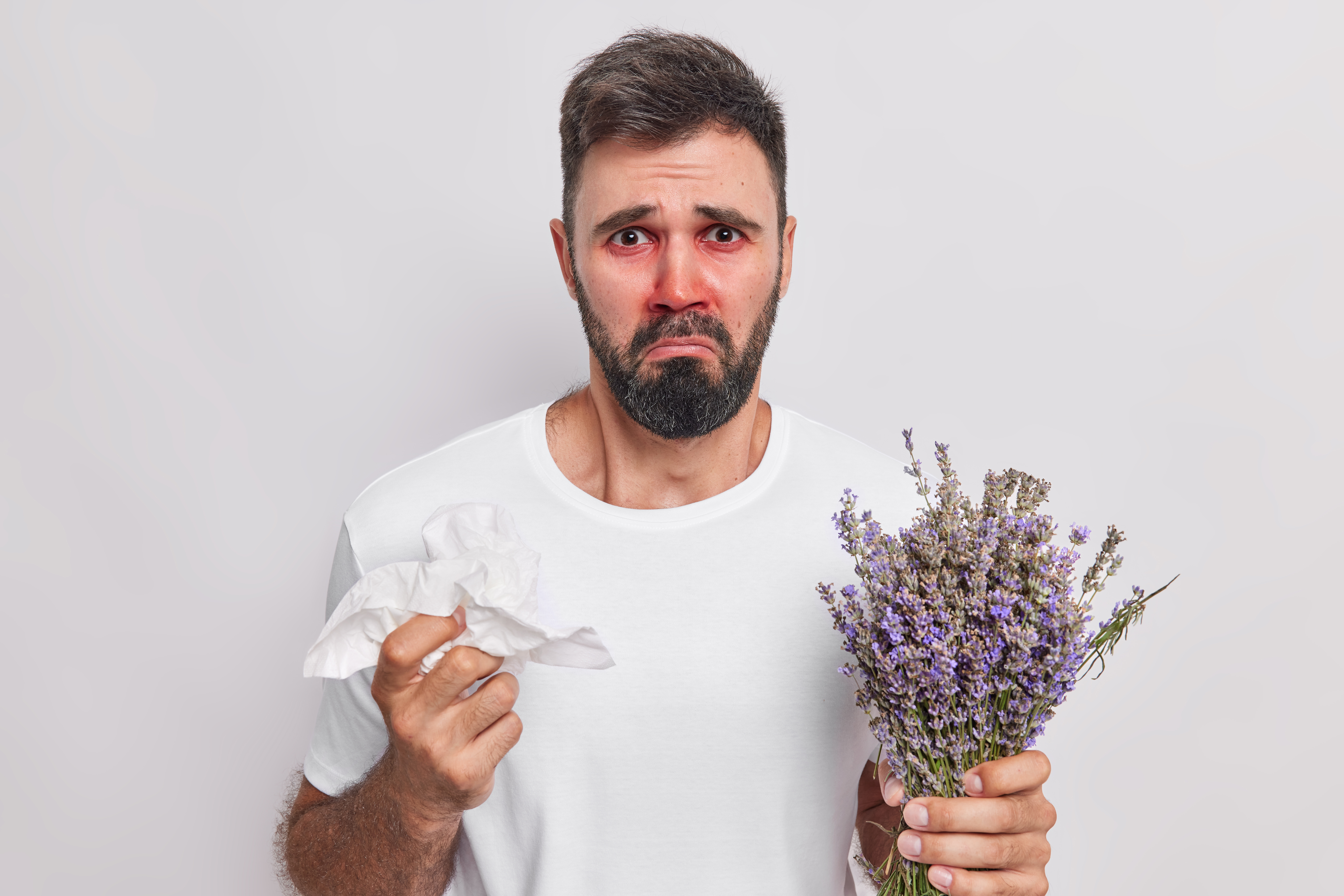 A man experiencing allergy symptoms such as red, irritated eyes and nasal discomfort while holding flowers