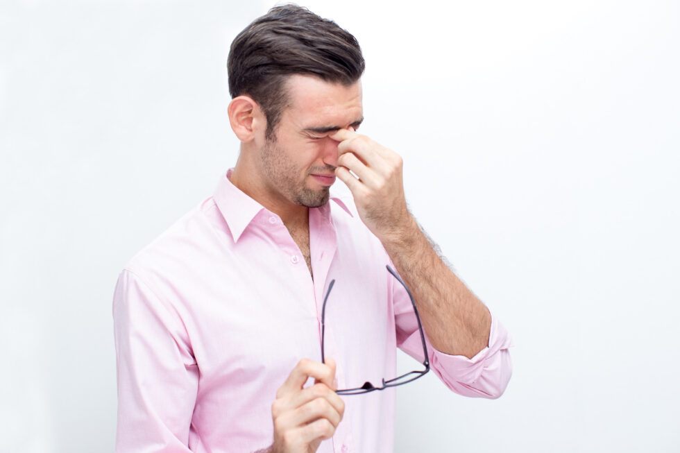 a man experiencing nasal discomfort, pinching the bridge of his nose while squinting in discomfort.
