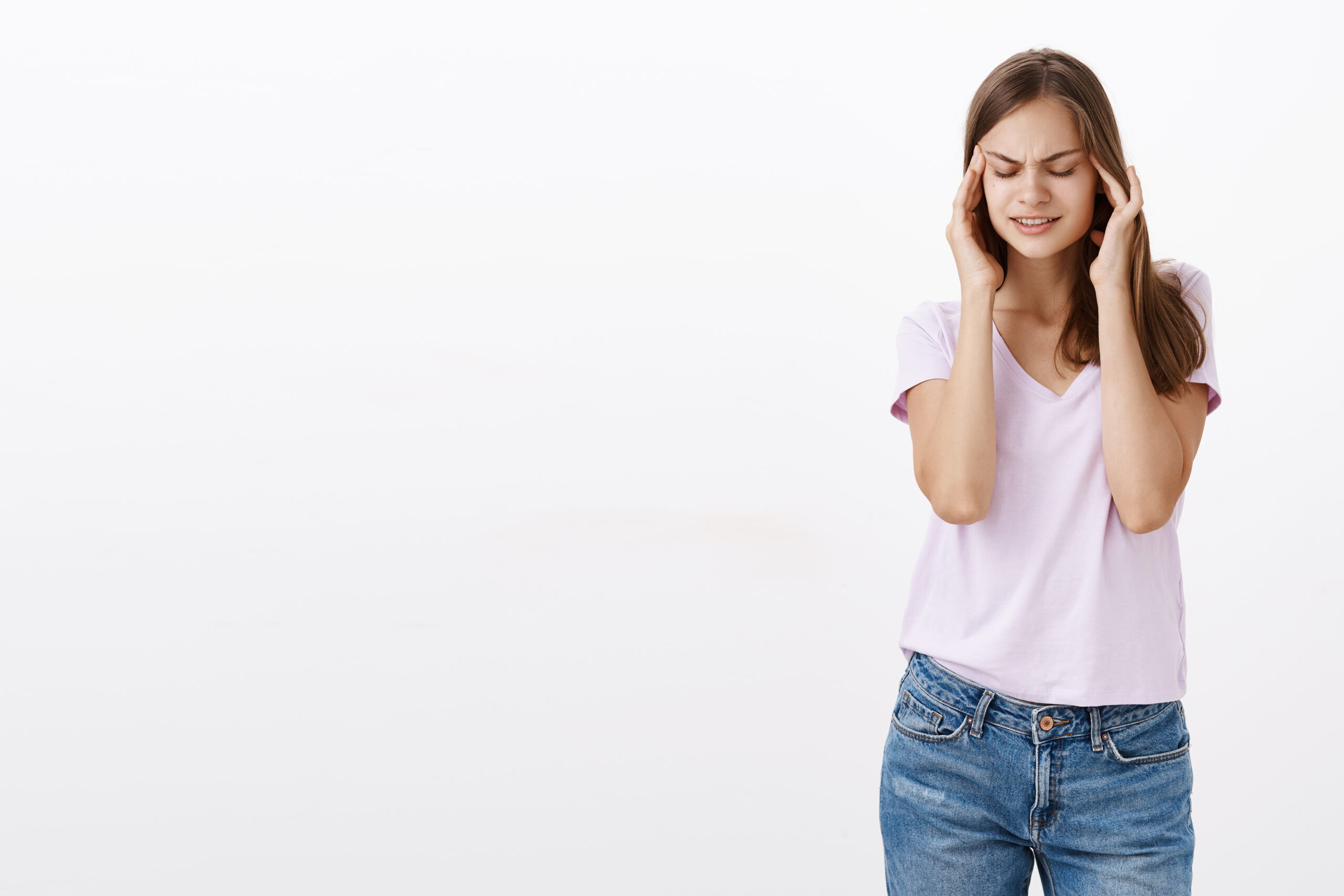a young woman experiencing dizziness or a headache, holding both sides of her head with a distressed expression against a clean white background.