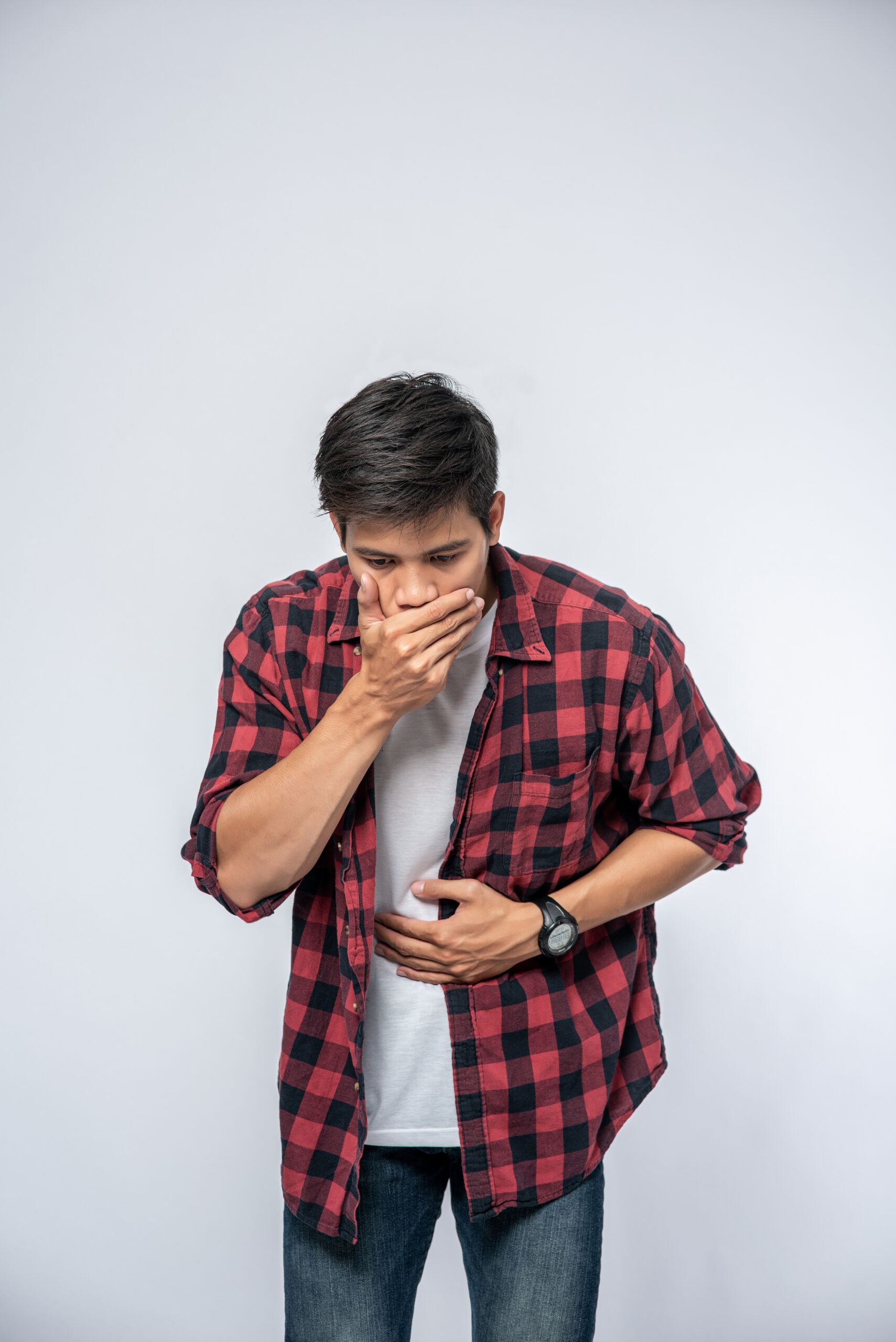 a young man experiencing nausea and stomach discomfort, covering his mouth while holding his abdomen.