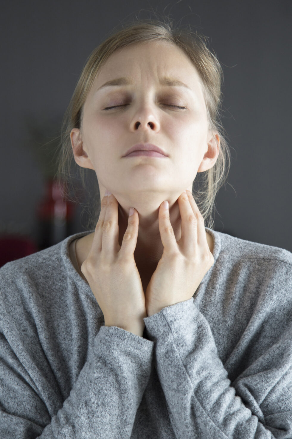 a woman experiencing throat or neck discomfort, gently touching the front of her neck with both hands.