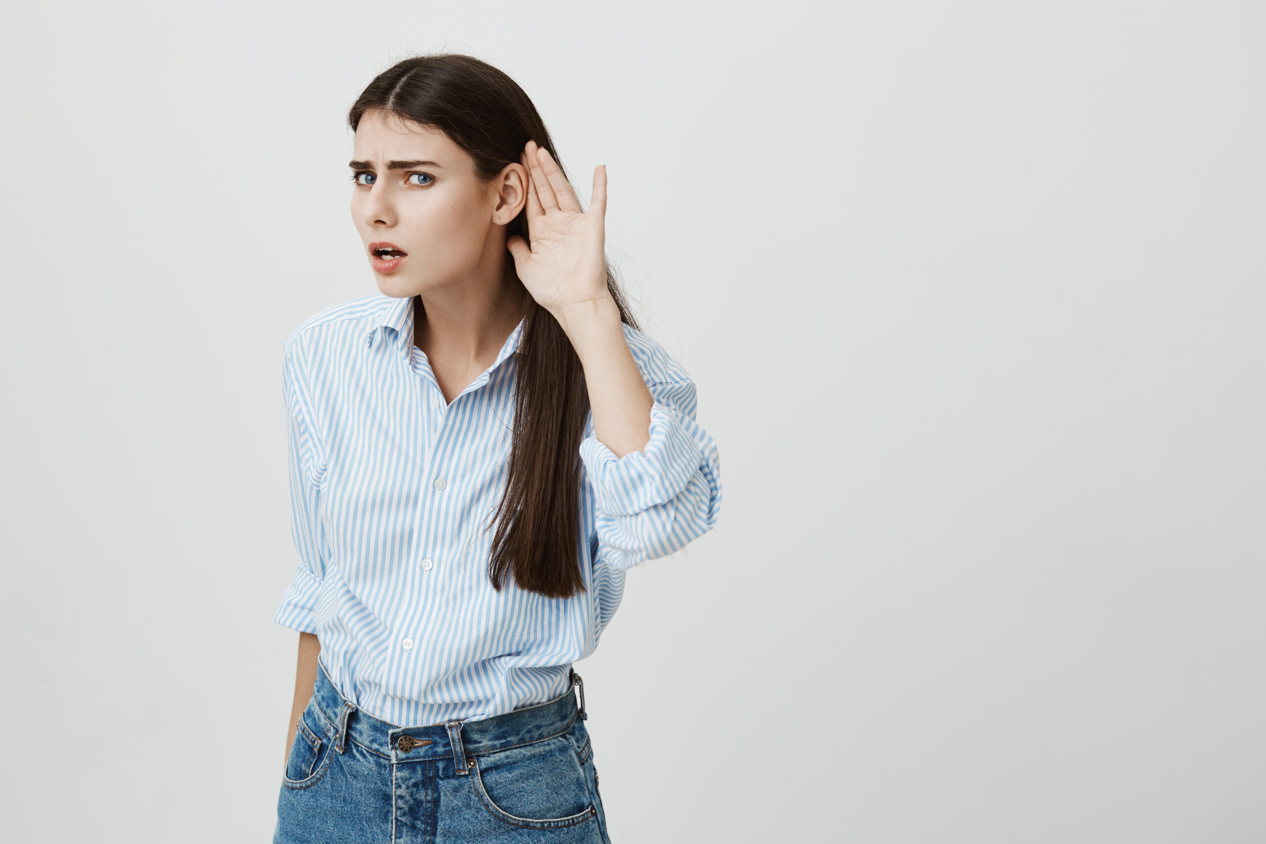 a woman cupping her ear and looking concerned because she is having difficulty hearing.