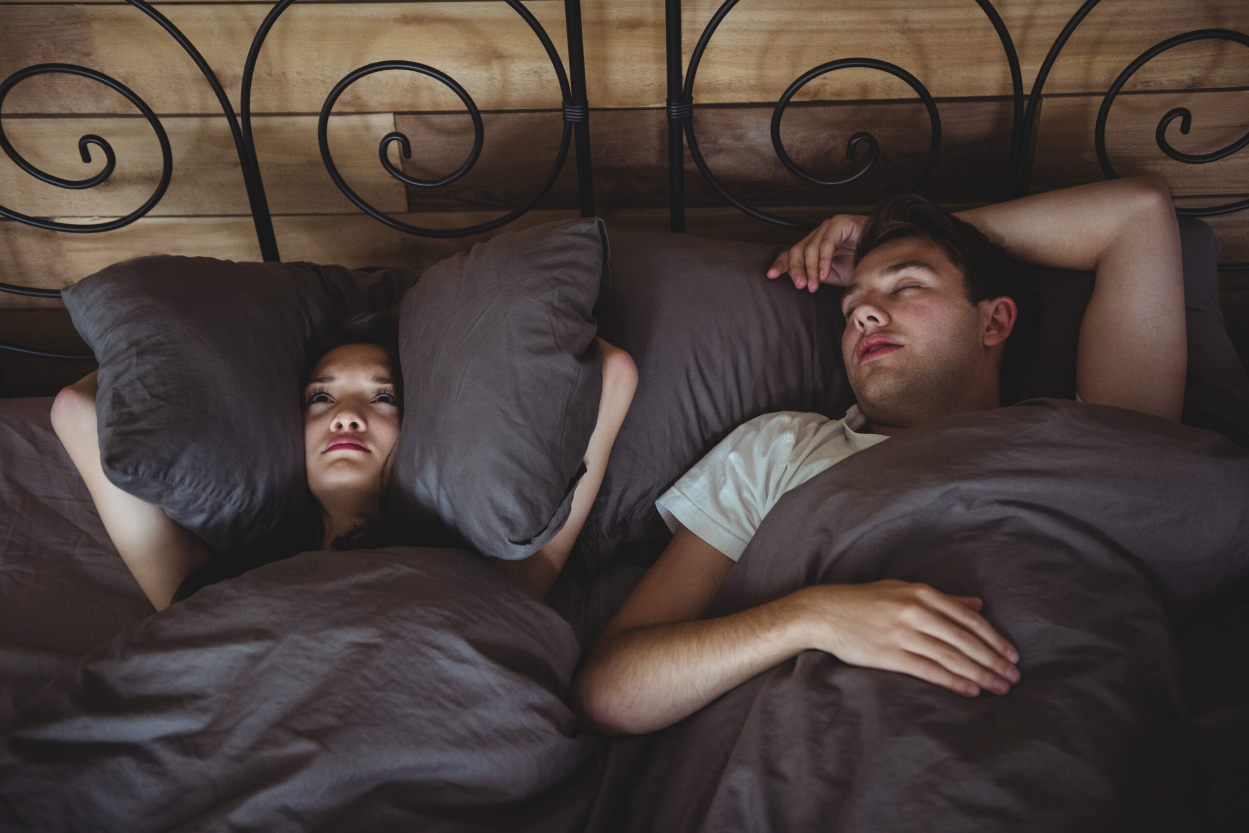 a couple experiencing disrupted sleep, with the woman appearing bothered while the man is asleep.