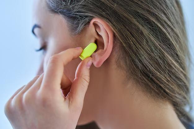 a woman inserting a yellow foam earplug into her ear.